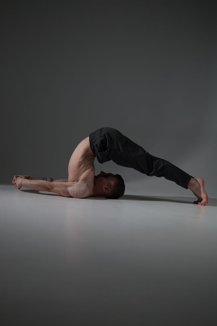 A man performing an advanced yoga position indoors on a serene background.