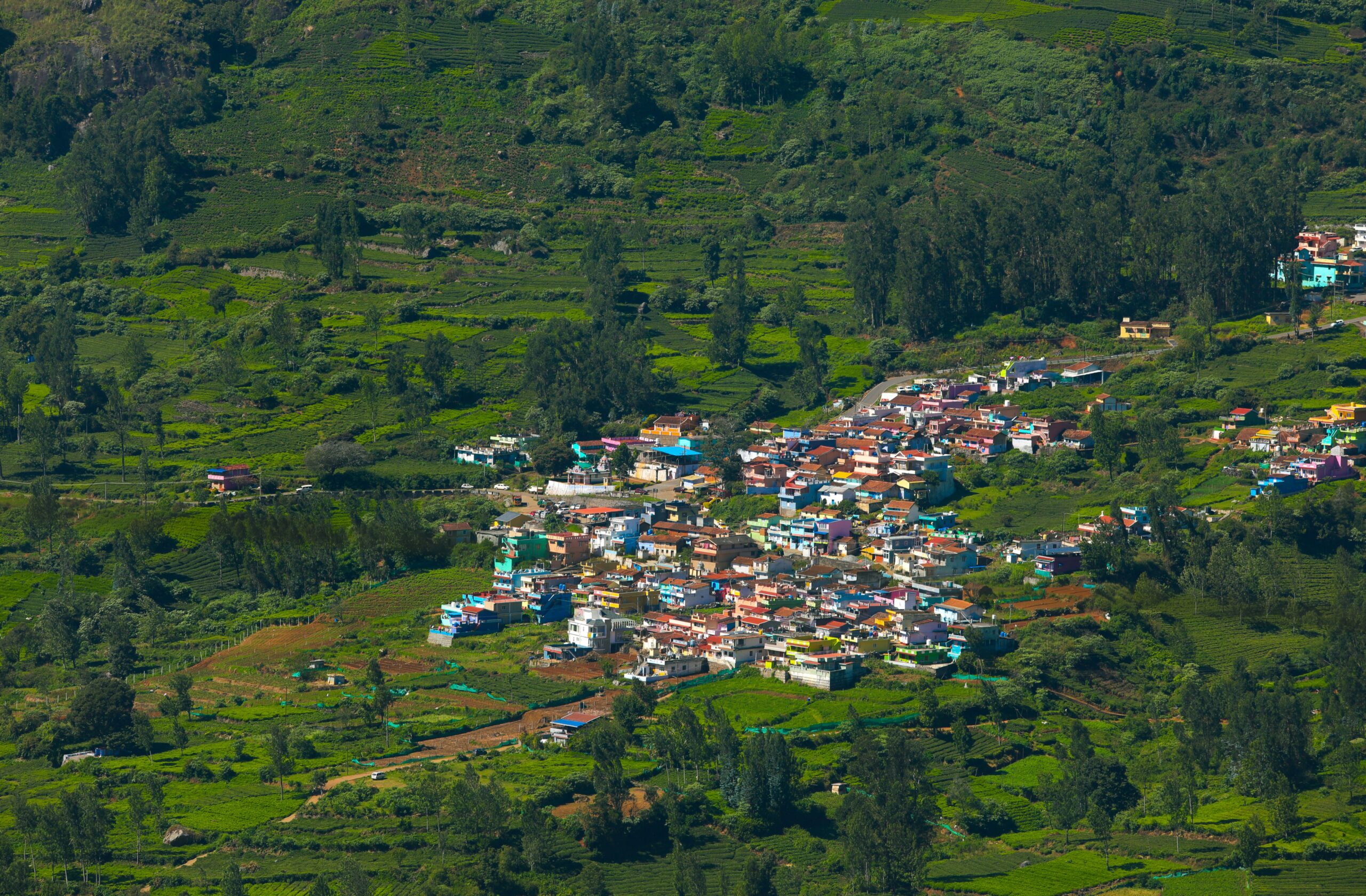 A colorful village nestled in a lush green valley, showcasing vibrant rooftops and natural scenery from above.
