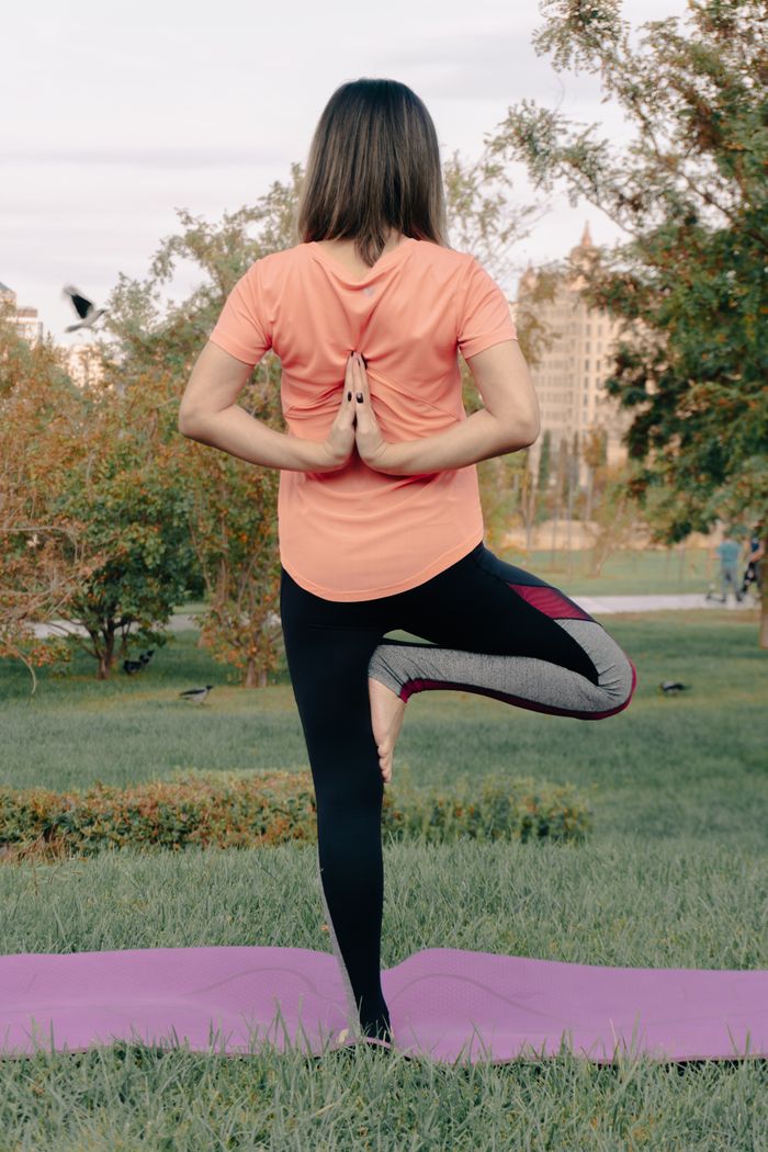 A woman performing a yoga pose outdoors on a purple mat in a tranquil park setting.